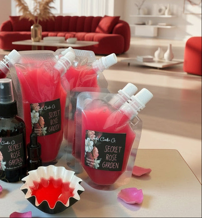 Bouquet of red squeezable wax melt bottles and a black bottle on a table with pink petals, against a neutral wall.