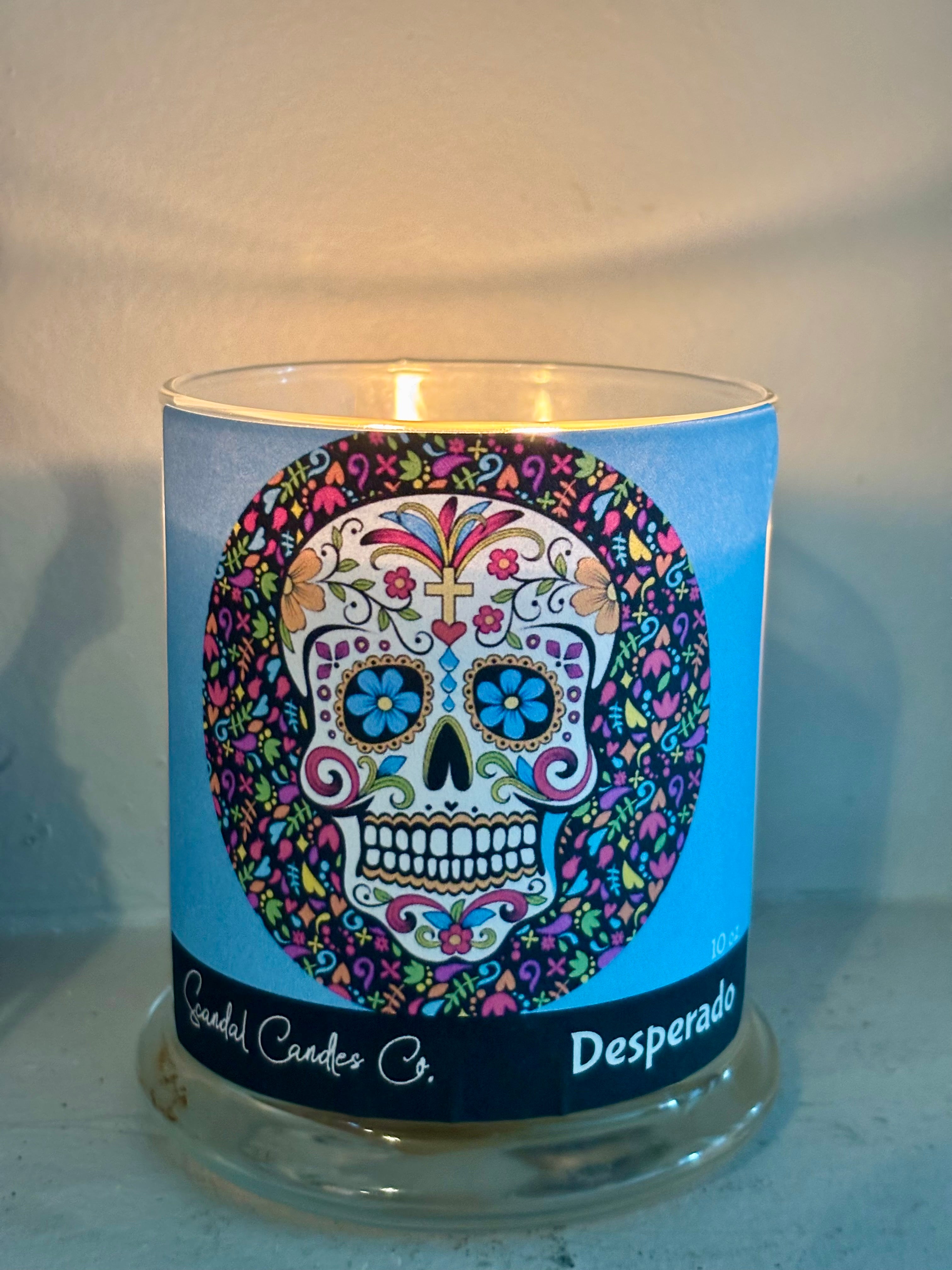 A glass jar candle with a blue label featuring a colorful sugar skull design and the text 'Candle Candles Co.' and 'Desperado'.