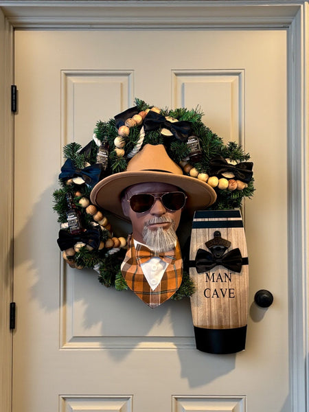 Decorative wreath with a man's head, hat, sunglasses, and 'Man Cave' sign on a door.