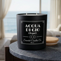 Acqua Di Gio (Type) black two-wick candle with corrected two-line label in a coastal setting
