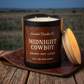 Open Midnight Cowboy candle with Texas leather label and two unlit wicks, wooden lid beside the jar in a ranch-inspired setting.