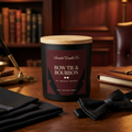 Bow Tie & Bourbon candle with burgundy After Hours label and wooden lid in a warm evening study with tuxedo fabric and bow tie.