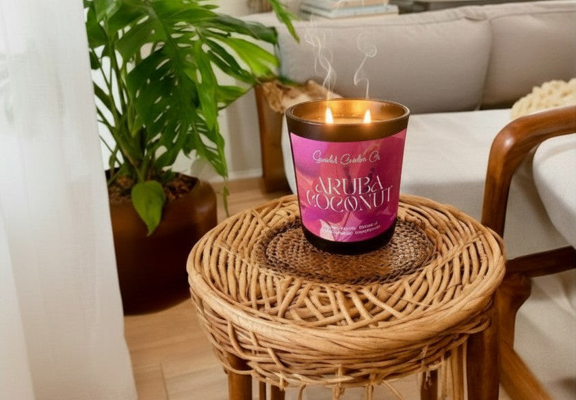 Scandal Candles Co. Aruba Coconut scented candle burning on a small wicker stool in a bright, tropical-inspired room.