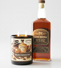 Scandal Candles Co. Bourbon Butterscotch two wick candle next to a bottle of bourbon whiskey on a white background.