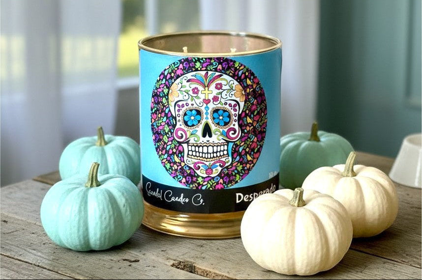 Scandal Candles Co. Desperado candle with sugar skull label surrounded by small blue and white pumpkins on a table