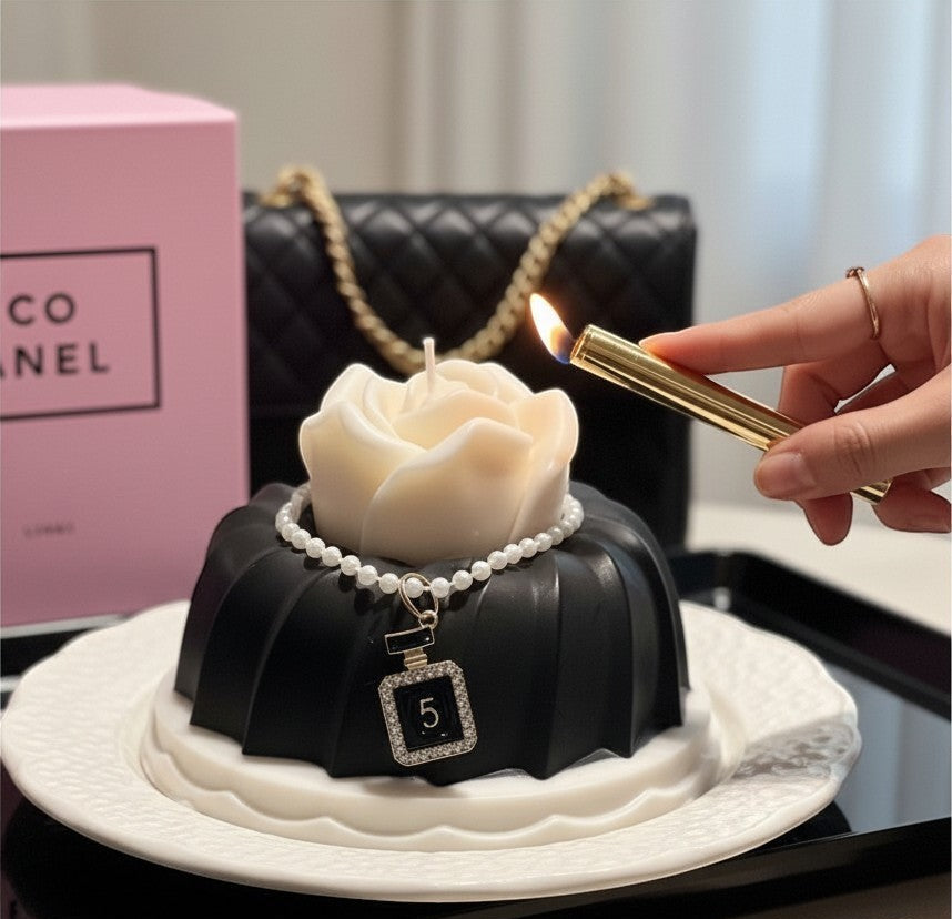Scandal Candles Co. rose-shaped candle with black tiered base, pearl necklace, and perfume bottle charm being lit.
